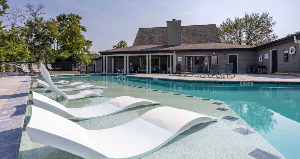 A pool with a white lounger in the foreground and a house in the background.