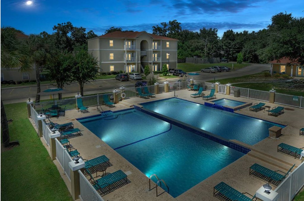 A large swimming pool surrounded by lounge chairs and a building in the background.