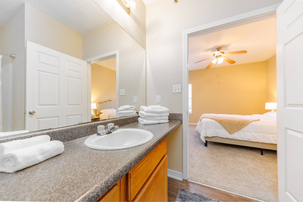 A bathroom with a sink, mirror, and a bedroom in the background.