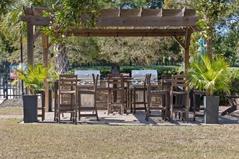 A wooden pergola with chairs and tables is surrounded by greenery at The Preserve at Pine Valley Apartments, Wilmington