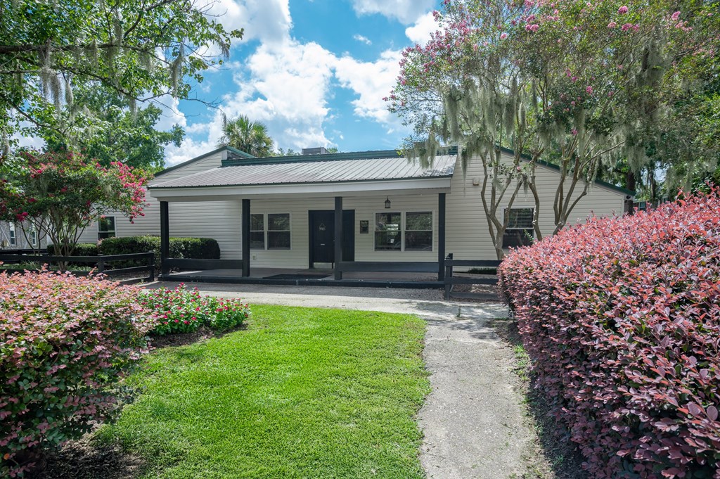A white house with a green lawn and pink flowers in front at Brackenbrook Apartments, North Charleston, SC, 29418