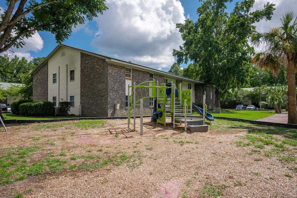 A playground with a slide and swings is in front of a brick building at Brackenbrook Apartments, North Charleston