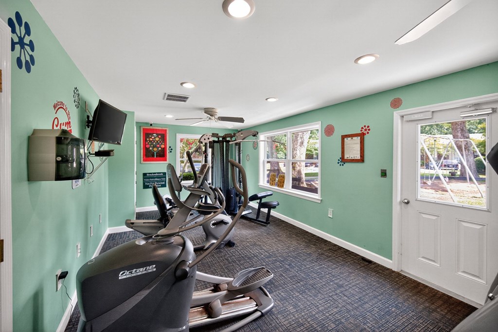A gym with exercise equipment and a window showing an outdoor scene at Brackenbrook Apartments, North Charleston, SC