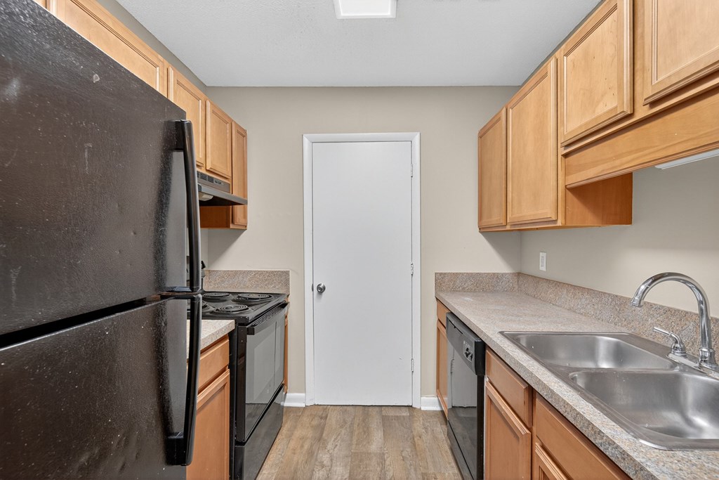 A kitchen with a black refrigerator, wooden cabinets, and a white door at Brackenbrook Apartments, North Charleston
