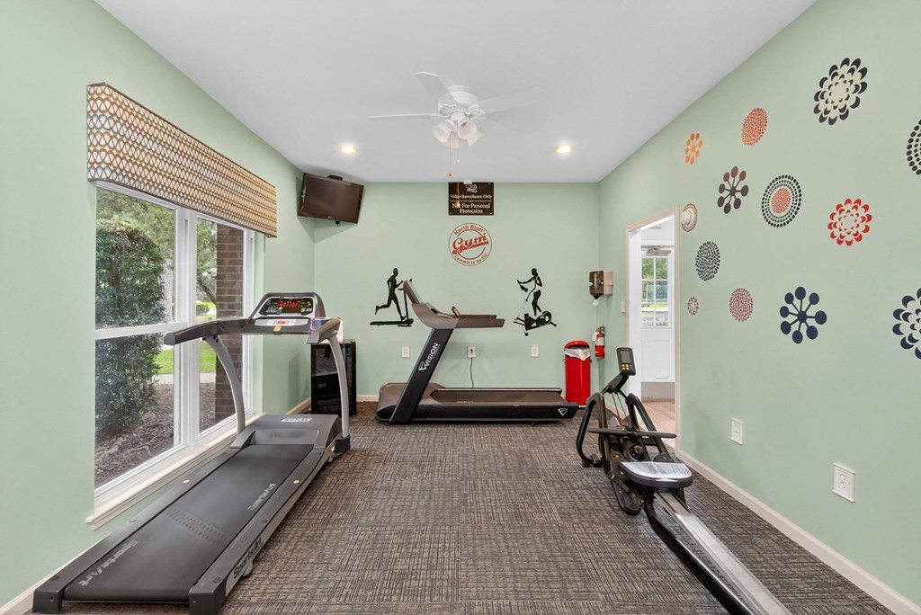 A gym with a treadmill, exercise bike, and wall decorations at North Bluff Apartments, North Charleston, SC