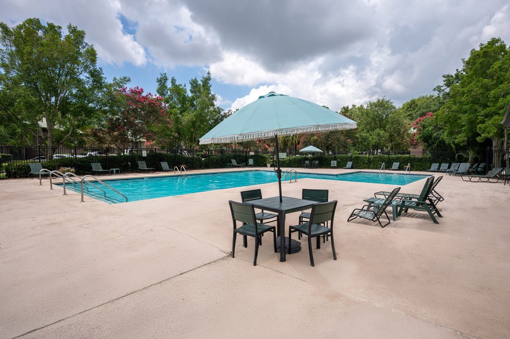 A pool with chairs and a table under an umbrella at North Bluff Apartments, North Charleston, South Carolina