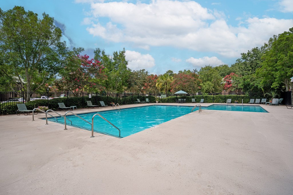 A large outdoor swimming pool surrounded by trees and lounge chairs at North Bluff Apartments, South Carolina