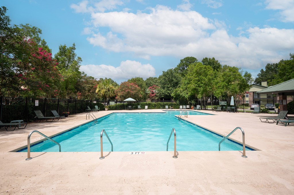 A large swimming pool surrounded by trees and a fence at North Bluff Apartments, North Charleston