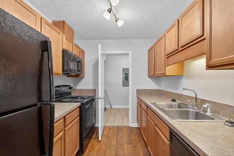 A kitchen with a black refrigerator and brown cabinets.