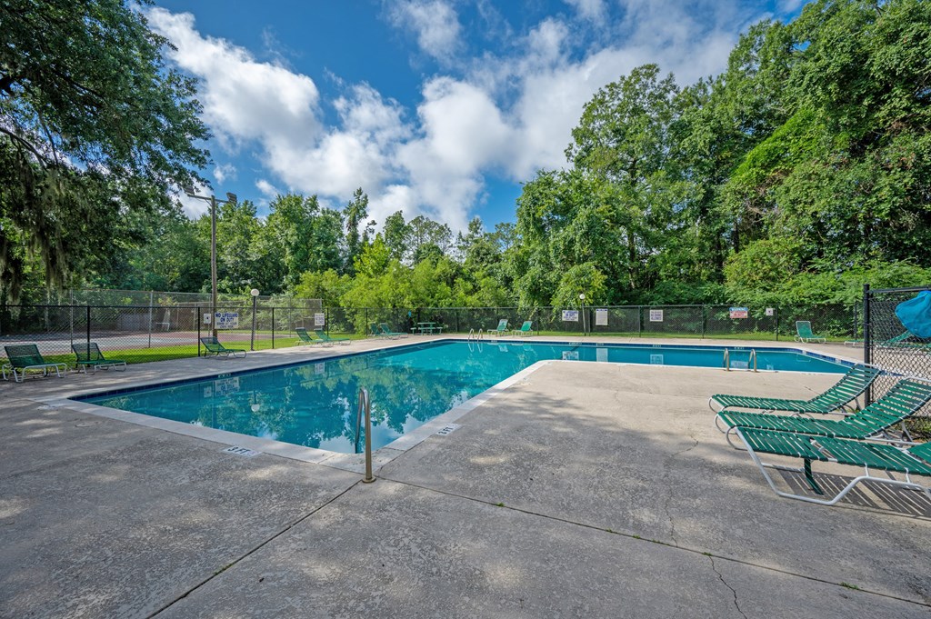 A large outdoor swimming pool surrounded by trees and a fence at Sawbranch Apartments, South Carolina