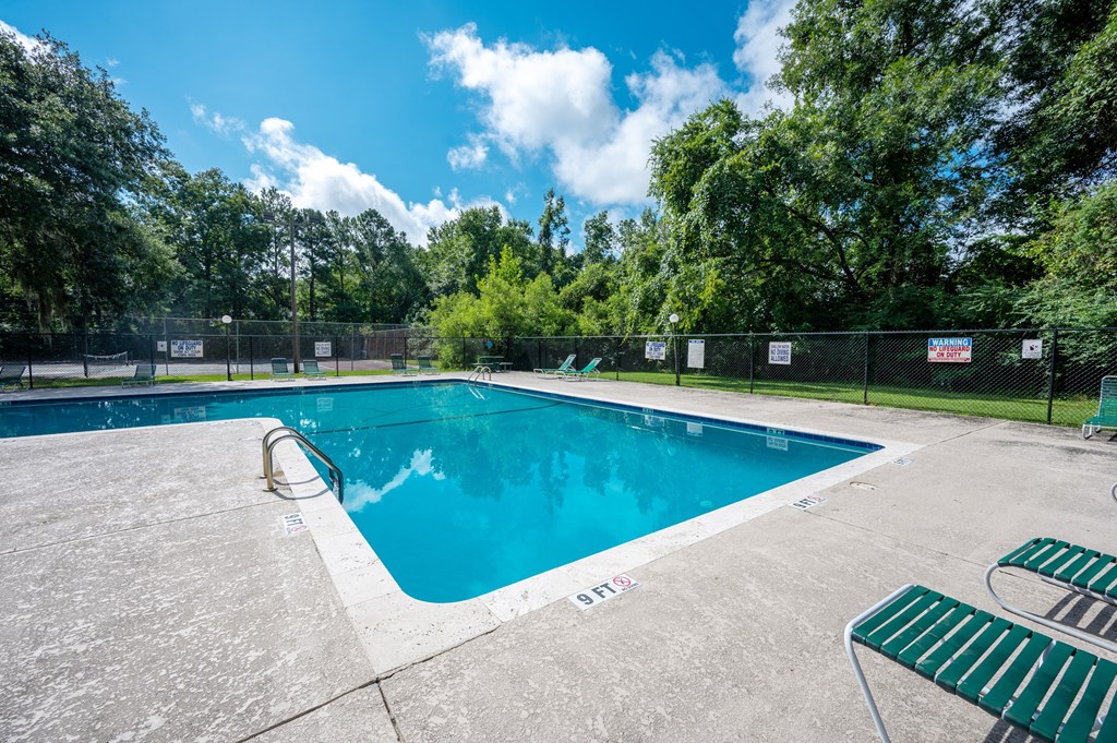A large outdoor swimming pool surrounded by a fence and trees at Sawbranch Apartments, Summerville