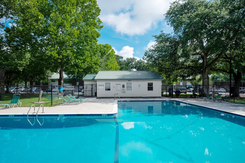 A swimming pool surrounded by trees and a building in the background at Sawbranch Apartments, Summerville, SC, 29485