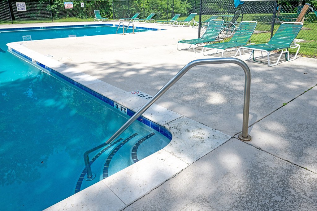 A pool with a metal ladder and green chairs at Sawbranch Apartments, Summerville 29485