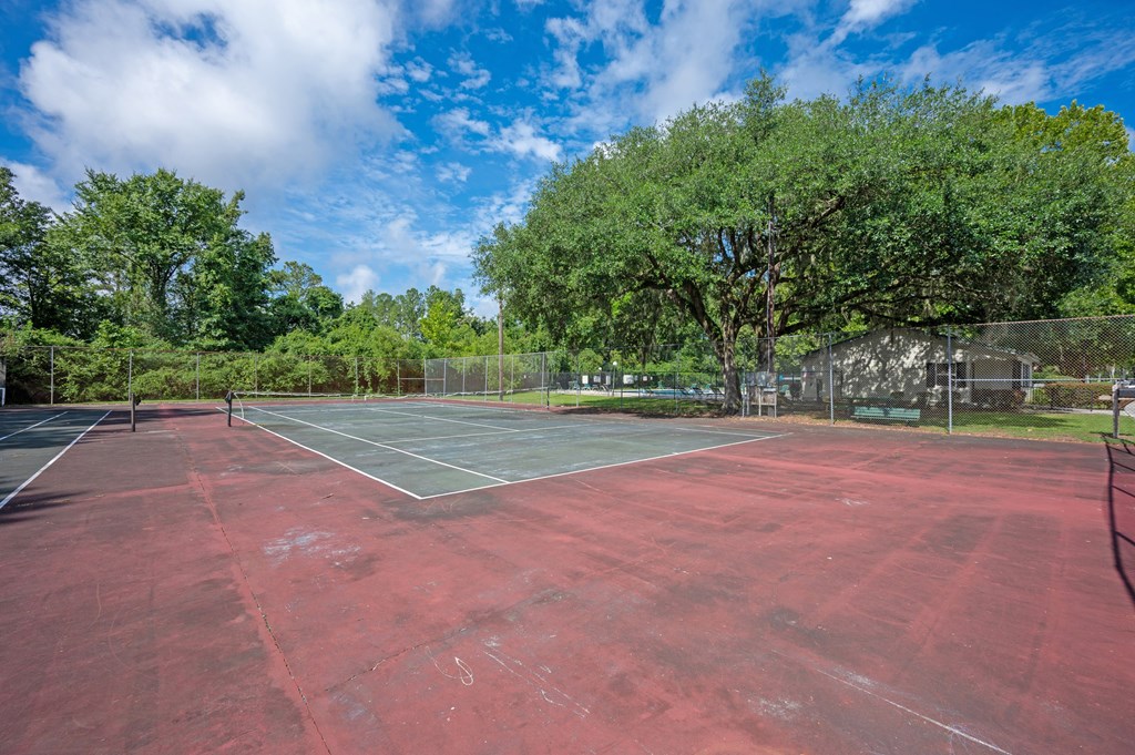 A red tennis court surrounded by trees and a fence at Sawbranch Apartments, Summerville
