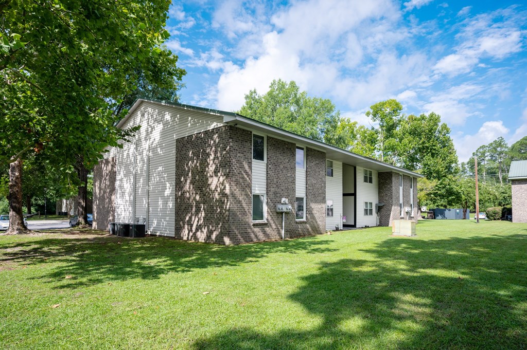 A house with a grey and white exterior is surrounded by a grassy lawn and trees at Sawbranch Apartments, Summerville, SC, 29485