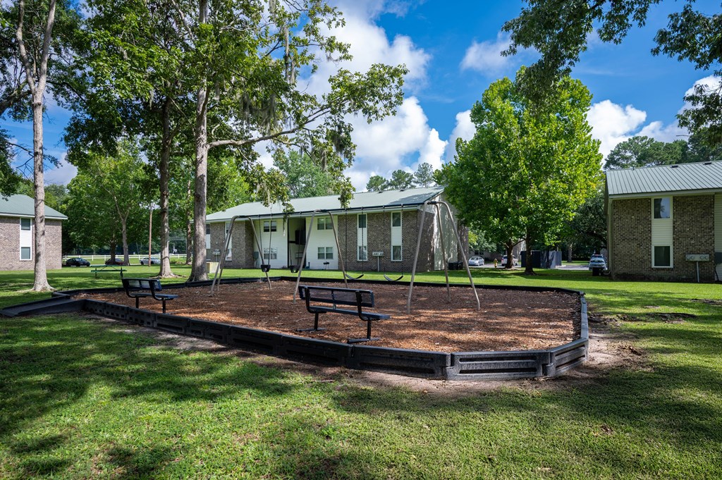 A playground with a slide and a swing set in a grassy area. at Sawbranch Apartments, Summerville 29485