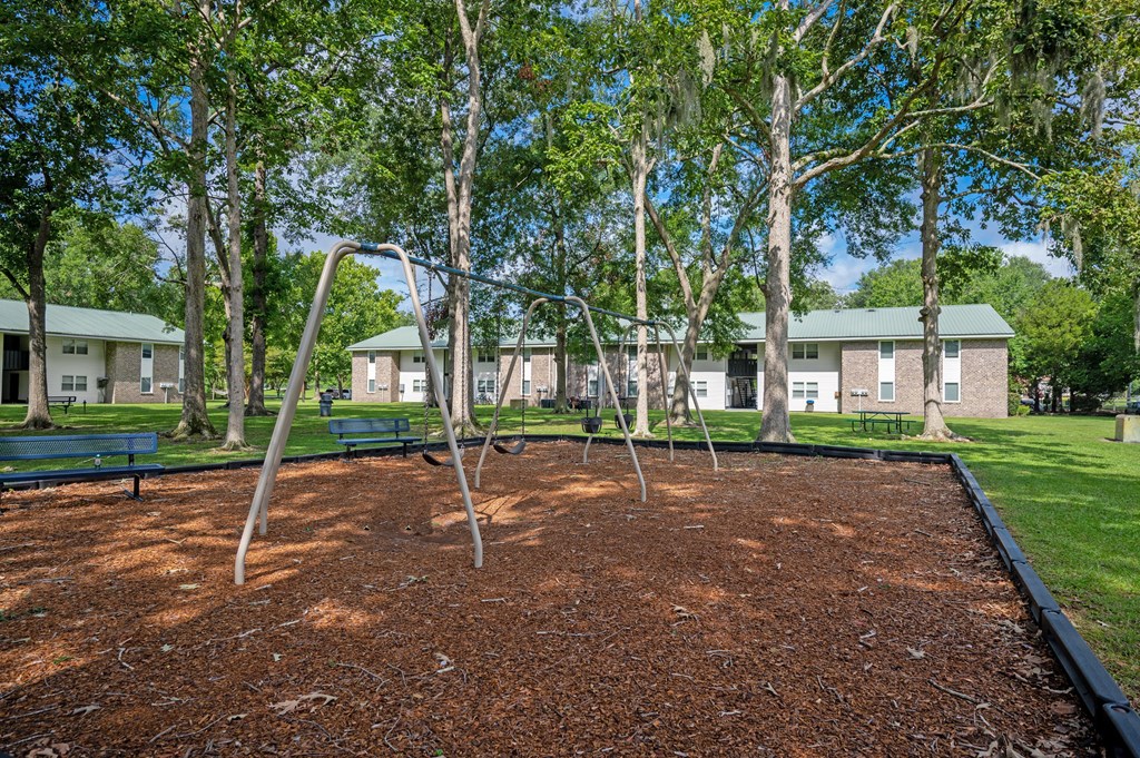 A playground with a red surface and a swing set. at Sawbranch Apartments, Summerville, SC, 29485