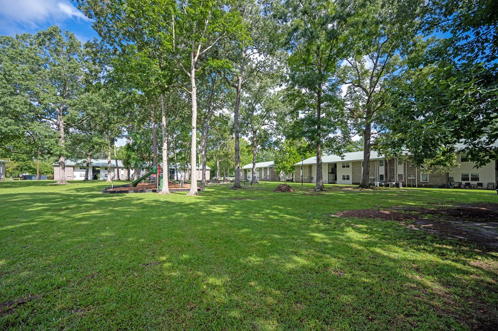 A large grassy area with trees and buildings in the background at Sawbranch Apartments, South Carolina, 29485