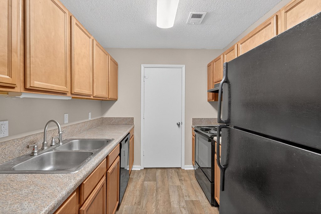 A kitchen with a black refrigerator and wooden cabinets at Sawbranch Apartments, Summerville, SC