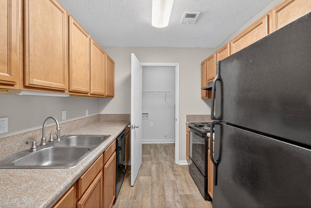 A kitchen with a black refrigerator, sink, and wooden cabinets at Sawbranch Apartments, Summerville