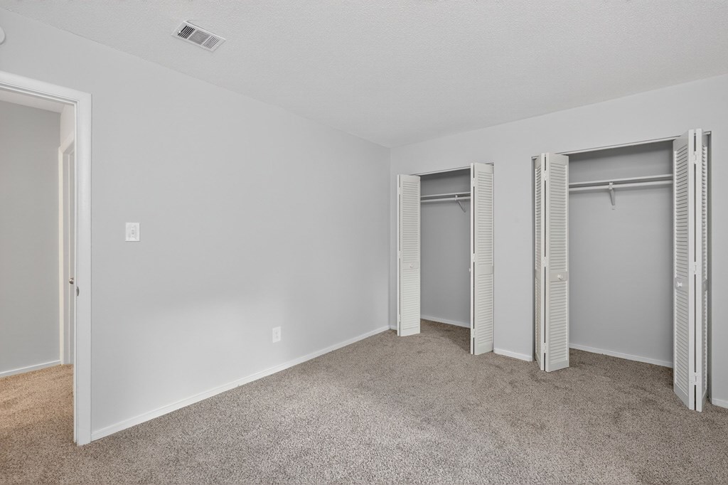 A room with white walls and carpeted floor with three open closets at Sawbranch Apartments, Summerville