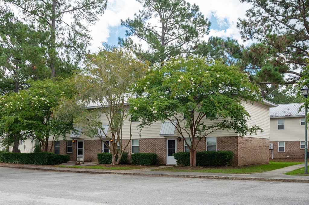 A building with a grey roof and a white door is surrounded by trees at The Landing Townhomes Apartments, South Carolina