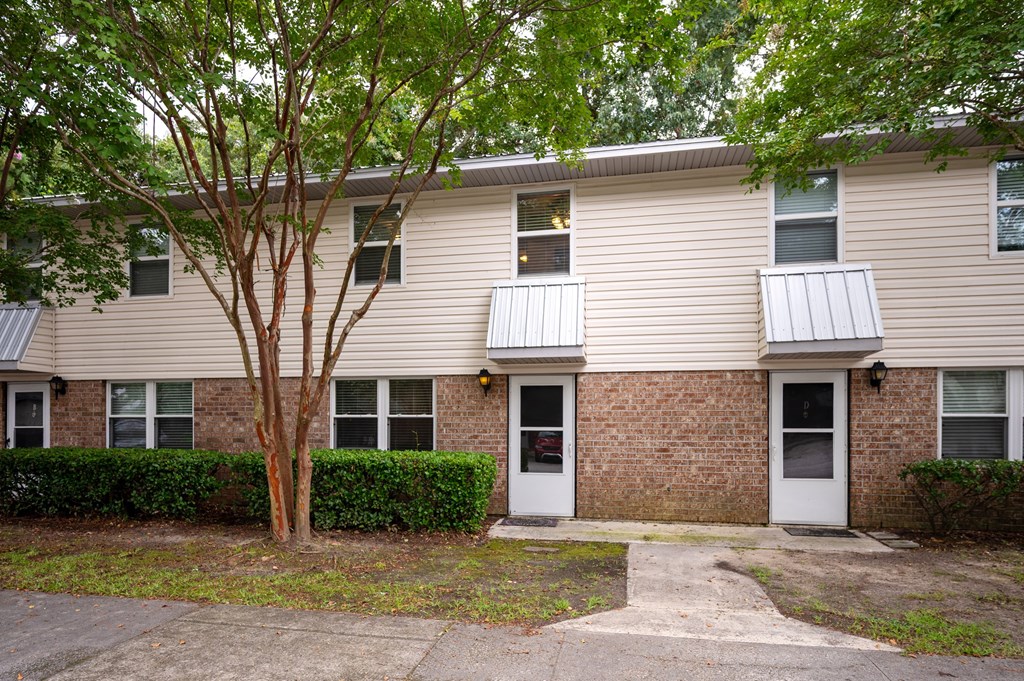 A tree in front of a tan building with a white door at The Landing Townhomes Apartments, Hanahan