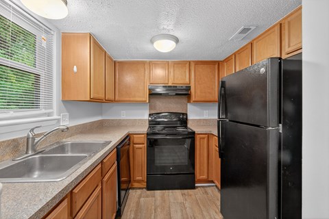 A black refrigerator stands in a kitchen with wooden cabinets and a stove.