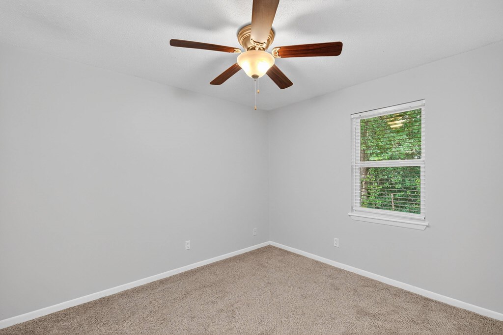 A room with a ceiling fan and a window showing greenery outside at The Landing Townhomes Apartments, Hanahan 29410