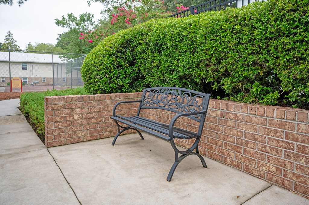 A black bench sits on a sidewalk next to a brick wall at Woodlocke Apartments, Moncks Corner, SC