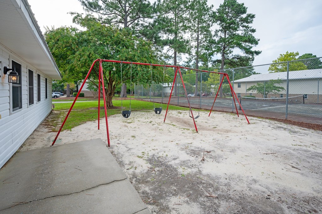 A red swing set sits in a sandy backyard at Woodlocke Apartments, Moncks Corner 27461