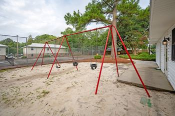 A red swing set sits in a sandy playground. at Woodlocke Apartments, South Carolina, 27461