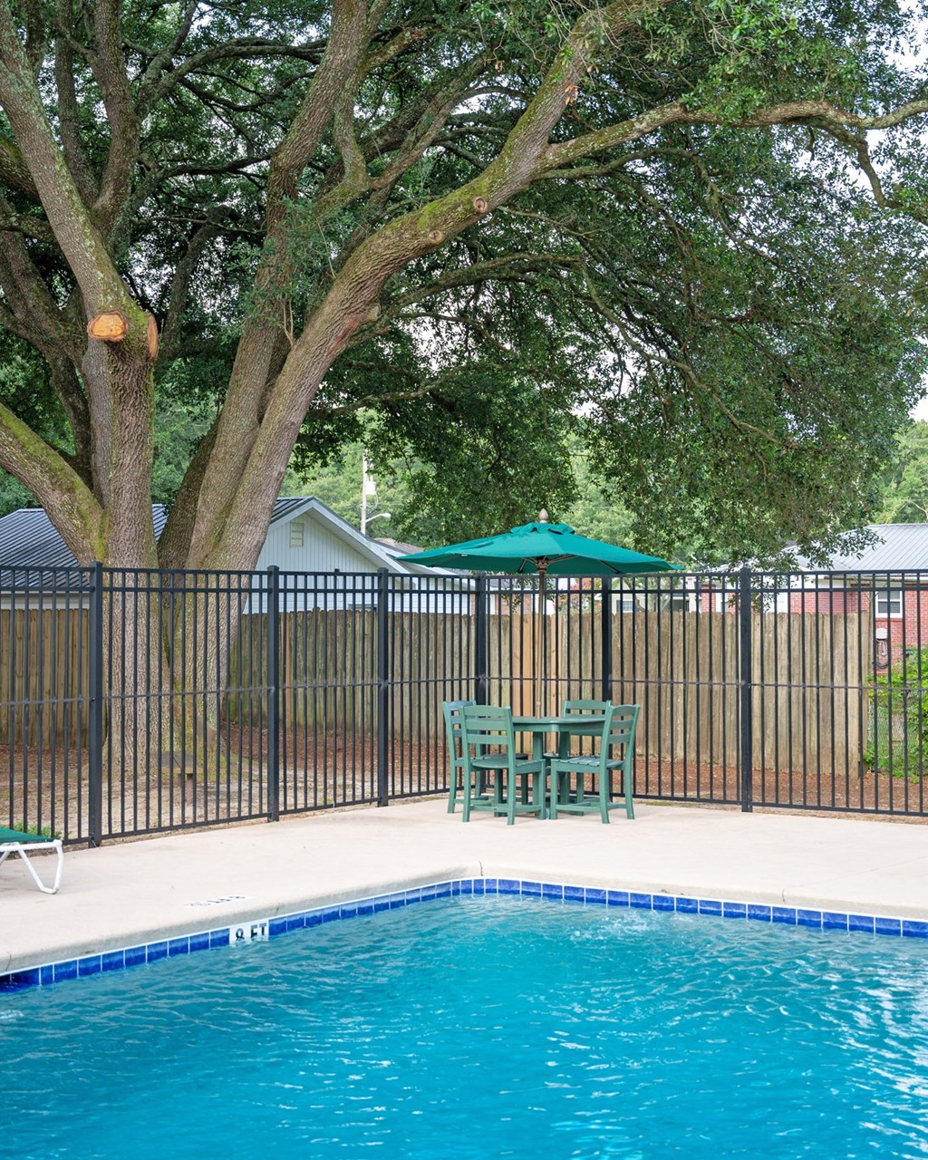A pool surrounded by a black fence and a green umbrella at Woodlocke Apartments, Moncks Corner 27461