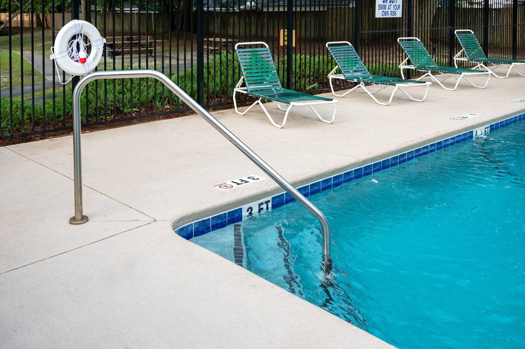 A pool with a metal railing and green chairs at Woodlocke Apartments, Moncks Corner, SC