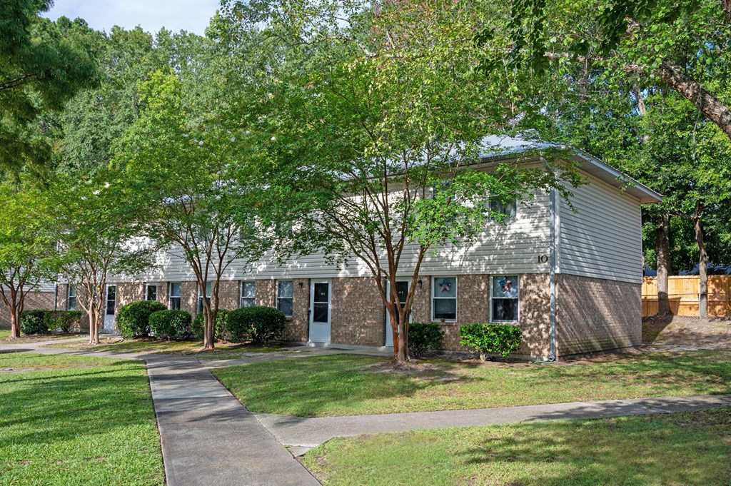 A tree-lined walkway leads to a small building at Woodlocke Apartments, Moncks Corner, SC, 27461