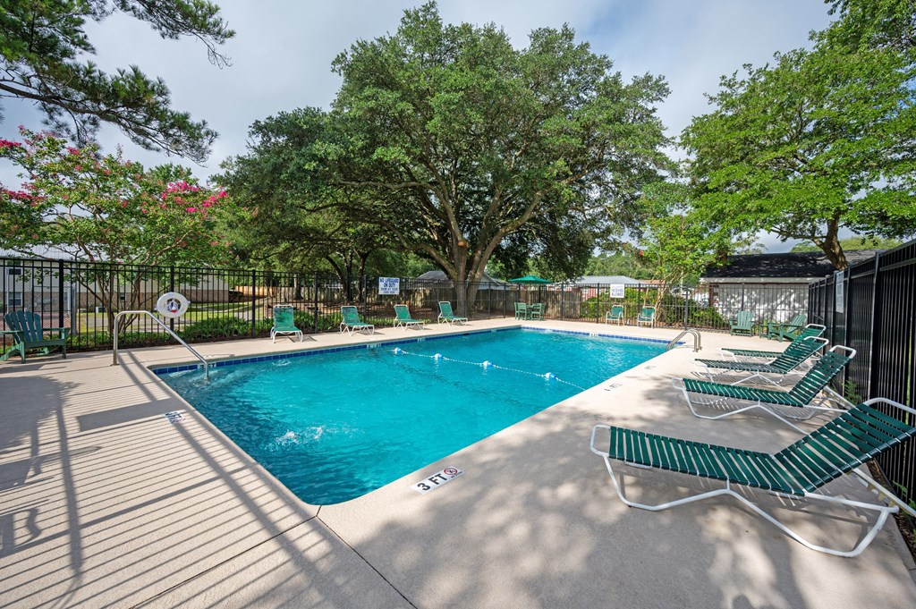 A pool surrounded by trees and chairs at Woodlocke Apartments, Moncks Corner