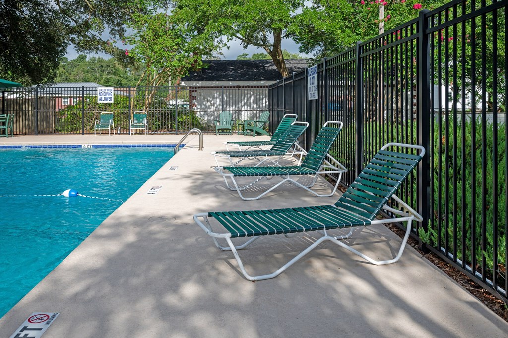 A pool with green chairs and a black fence at Woodlocke Apartments, Moncks Corner, SC, 27461