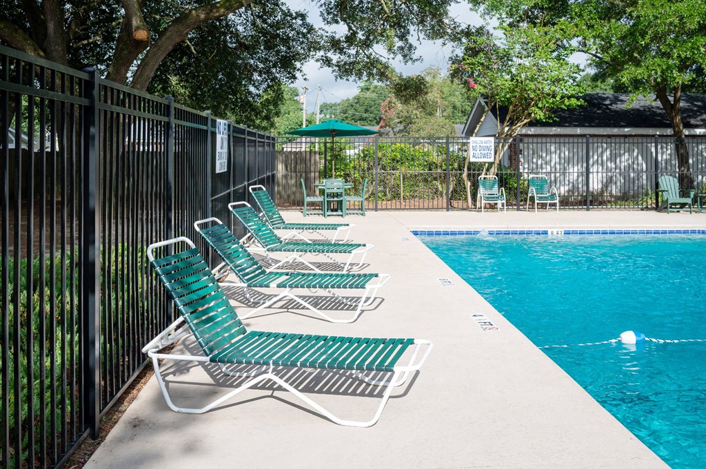 A poolside with green chairs and a black fence at Woodlocke Apartments, Moncks Corner, South Carolina