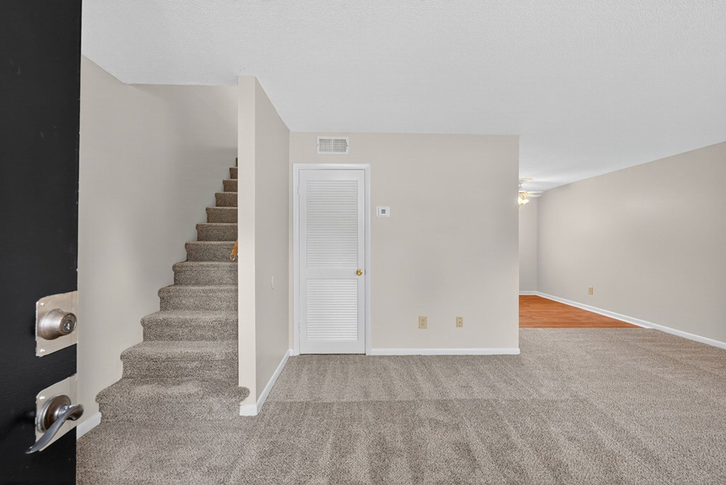 A hallway with a carpeted floor, a staircase, and a white door at Woodlocke Apartments, South Carolina