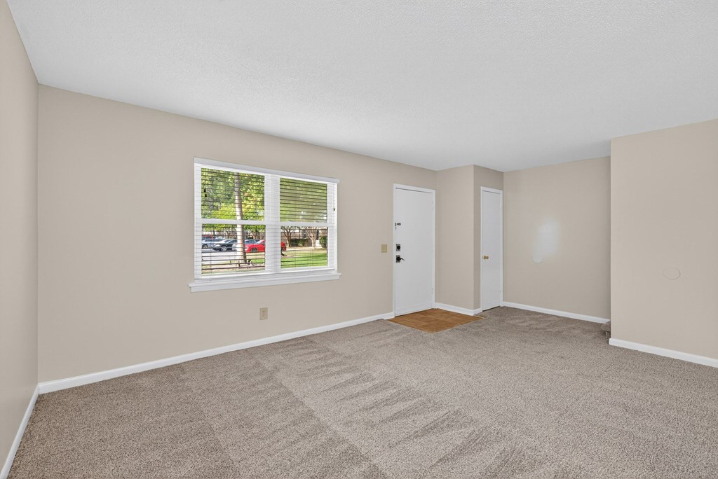 A room with a carpeted floor and a window showing a view of a yard at Woodlocke Apartments, Moncks Corner, SC