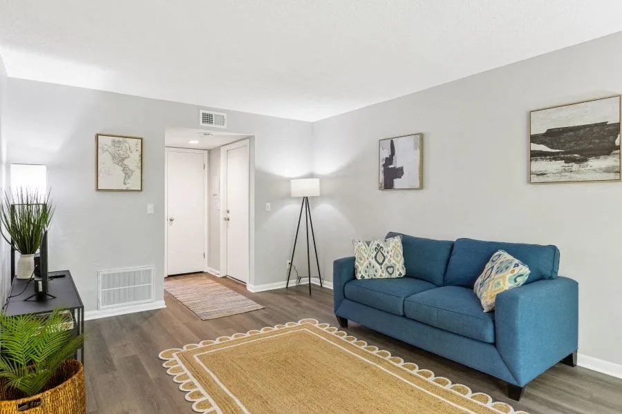 A blue couch with a white pillow is in the middle of a room with a rug at The Preserve at Pine Valley Apartments, Wilmington, NC 28412