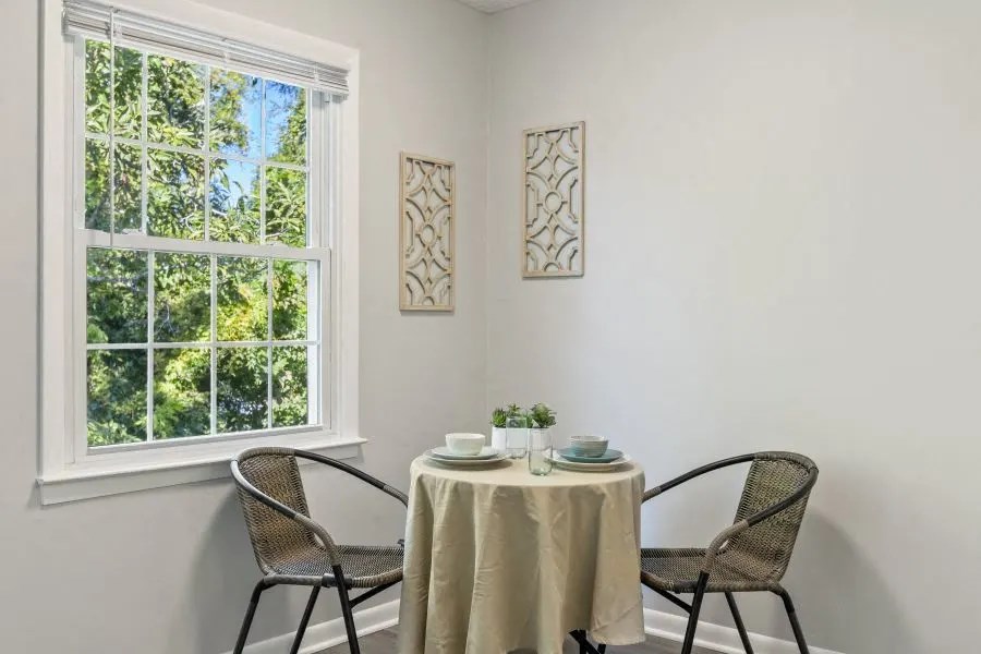 A table with a white tablecloth and two chairs is set up in front of a window at The Preserve at Pine Valley Apartments, North Carolina 28412