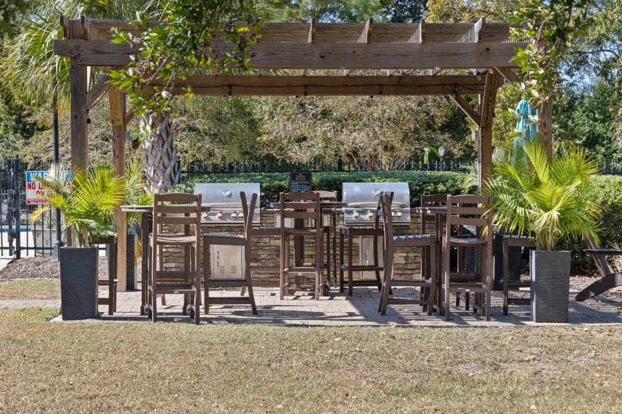 A wooden pergola with chairs and tables is surrounded by greenery at The Preserve at Pine Valley Apartments, North Carolina