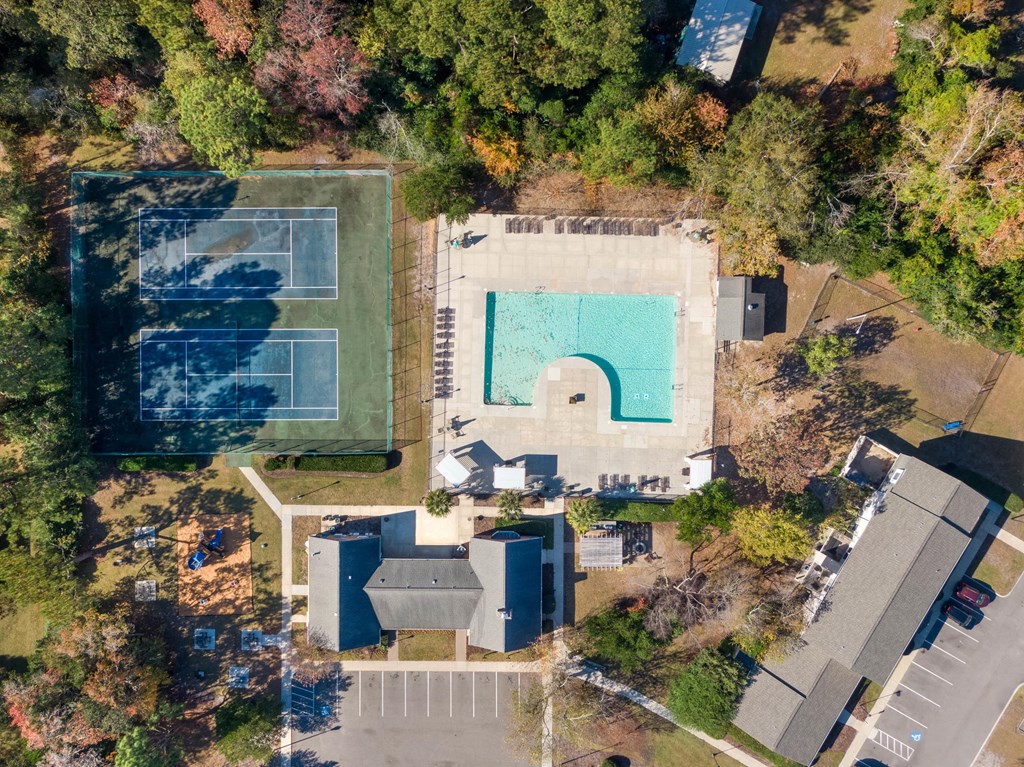 An aerial view of a tennis court and a swimming pool surrounded by trees and buildings at The Preserve at Pine Valley Apartments, Wilmington, 28412