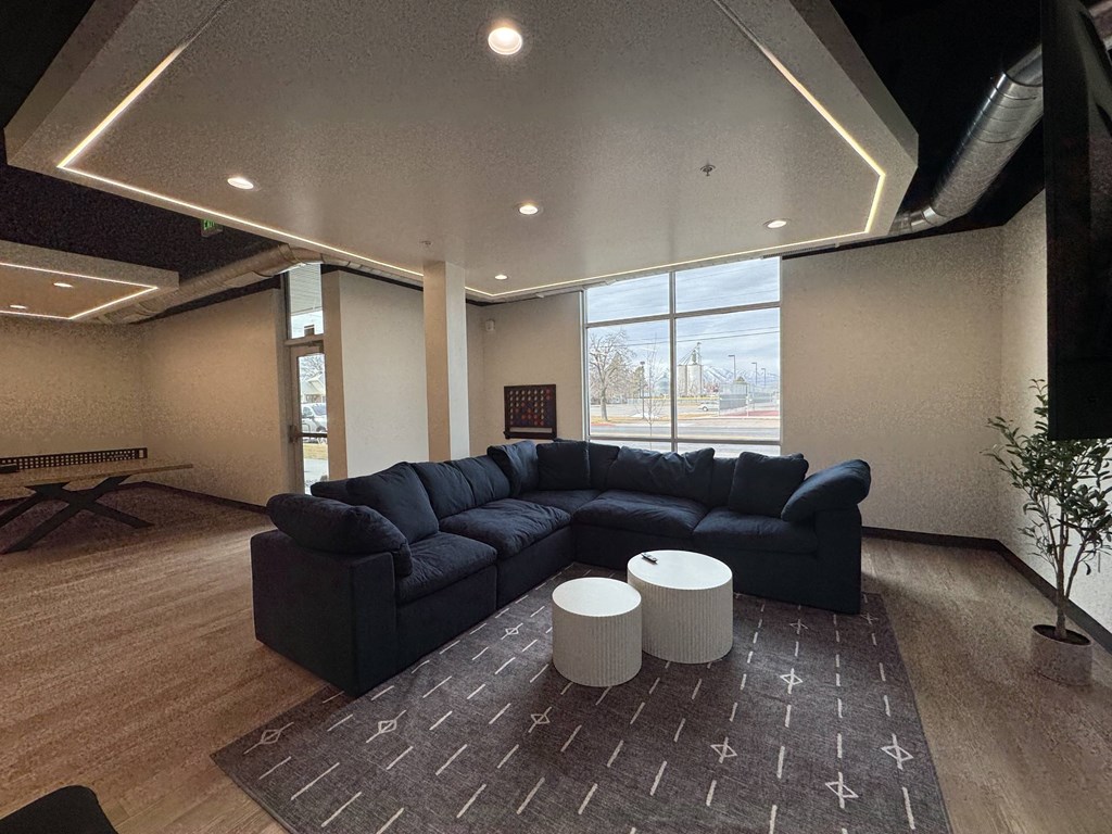 A black sectional sofa with a round ottoman in front of it.