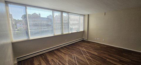 A room with wooden floors and a large window with blinds.