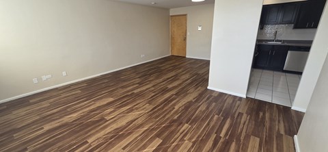 A room with wooden flooring and a door leading to a kitchen.