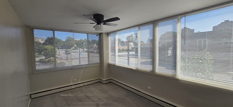 A room with a ceiling fan and large windows overlooking a street.