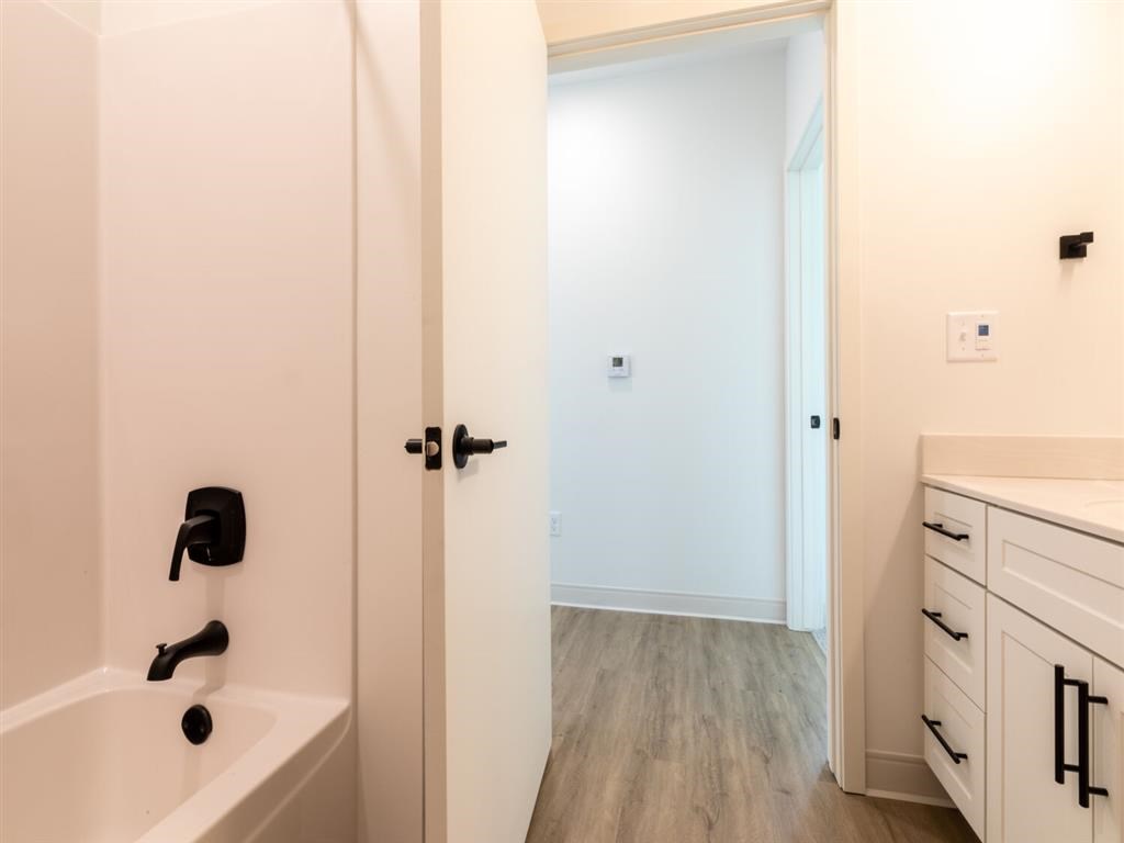 A white bathroom with a tub, sink, and wooden floors.