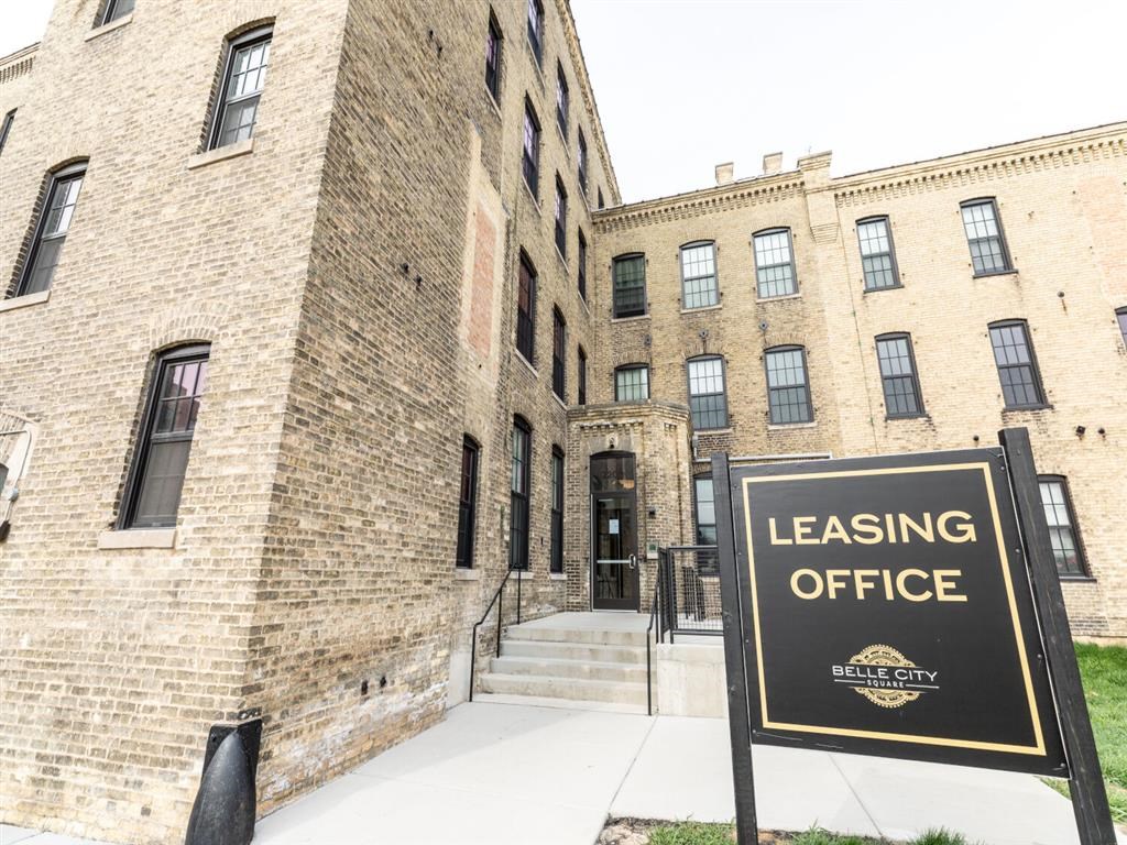A sign for a leasing office stands in front of a brick building.
